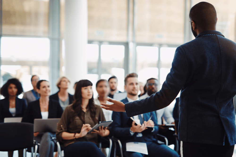 Employees sitting in a meeting intently watching a speaker in front of them.