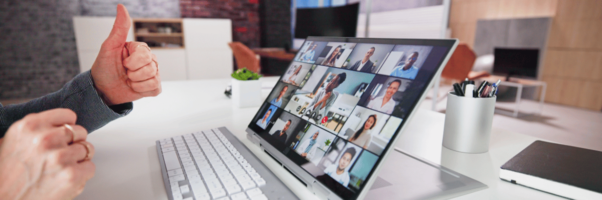 Person giving thumbs up during virtual meeting, laptop screen showing grid of video call participants