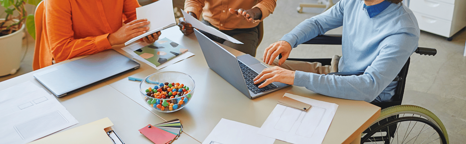 One employee in a wheelchair sits at a table, meeting with two other employees.